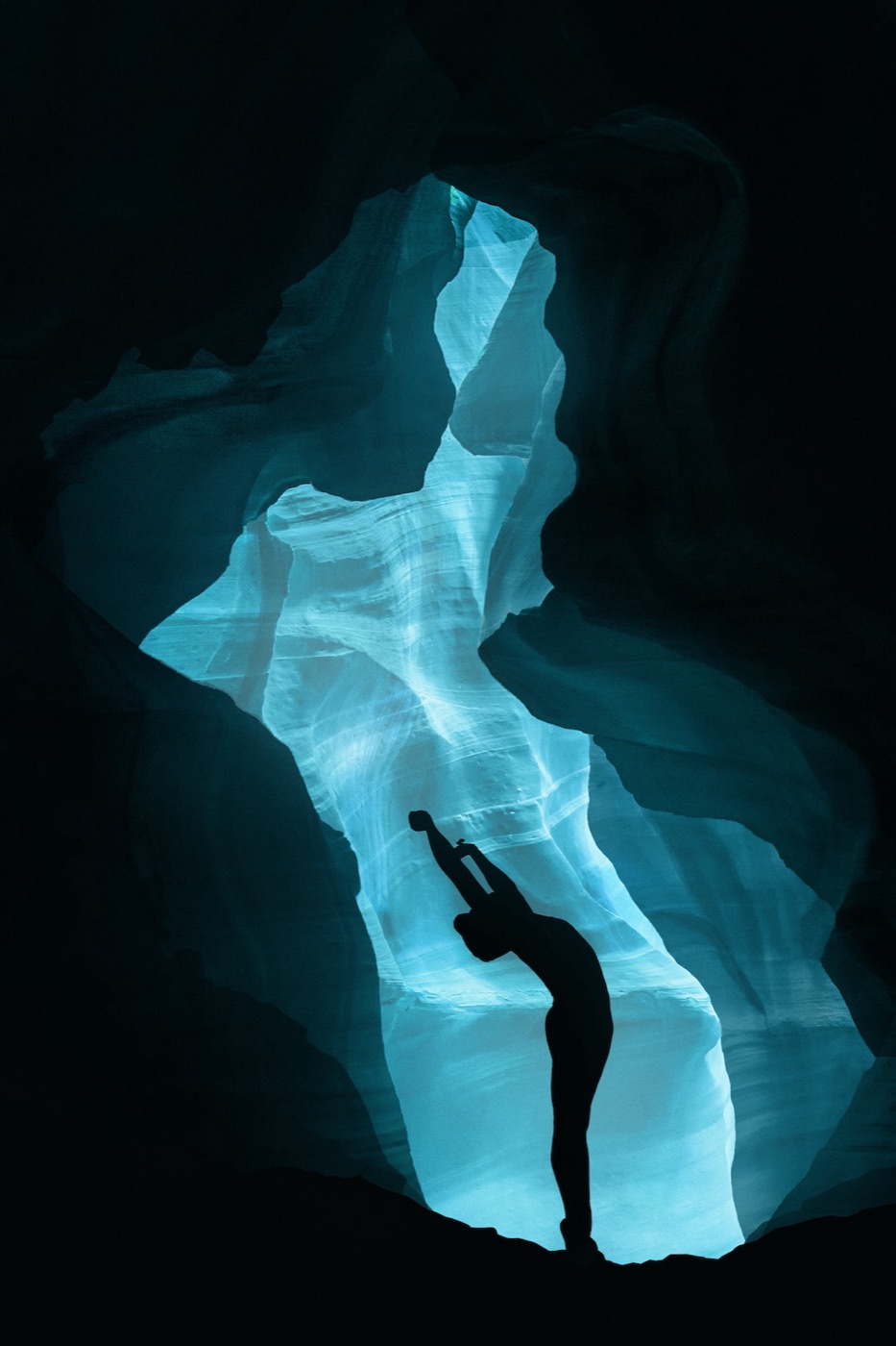 A figure in a backbend silhouetted against a lit slot canyon
